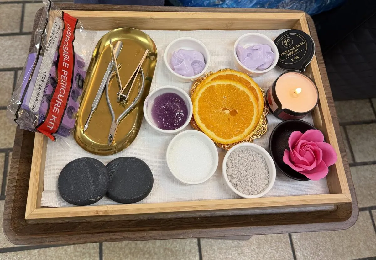 Pedicure tray with hot stones, orange slices, a lit massage candle, scrubs, masks, sanitised tools and a sealed disposable pedicure kit